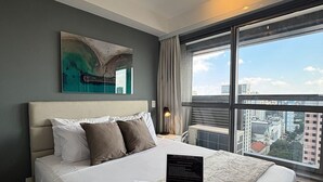 Habitación de hotel con una cama grande, vistas a la ciudad, un cuadro en la pared e información de la habitación en un cartel.