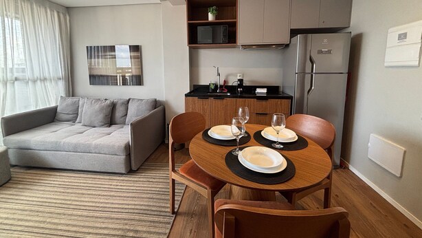 Una sala de estar moderna con un sofá, una mesa de comedor para dos personas y una zona de cocina con armarios y electrodomésticos.