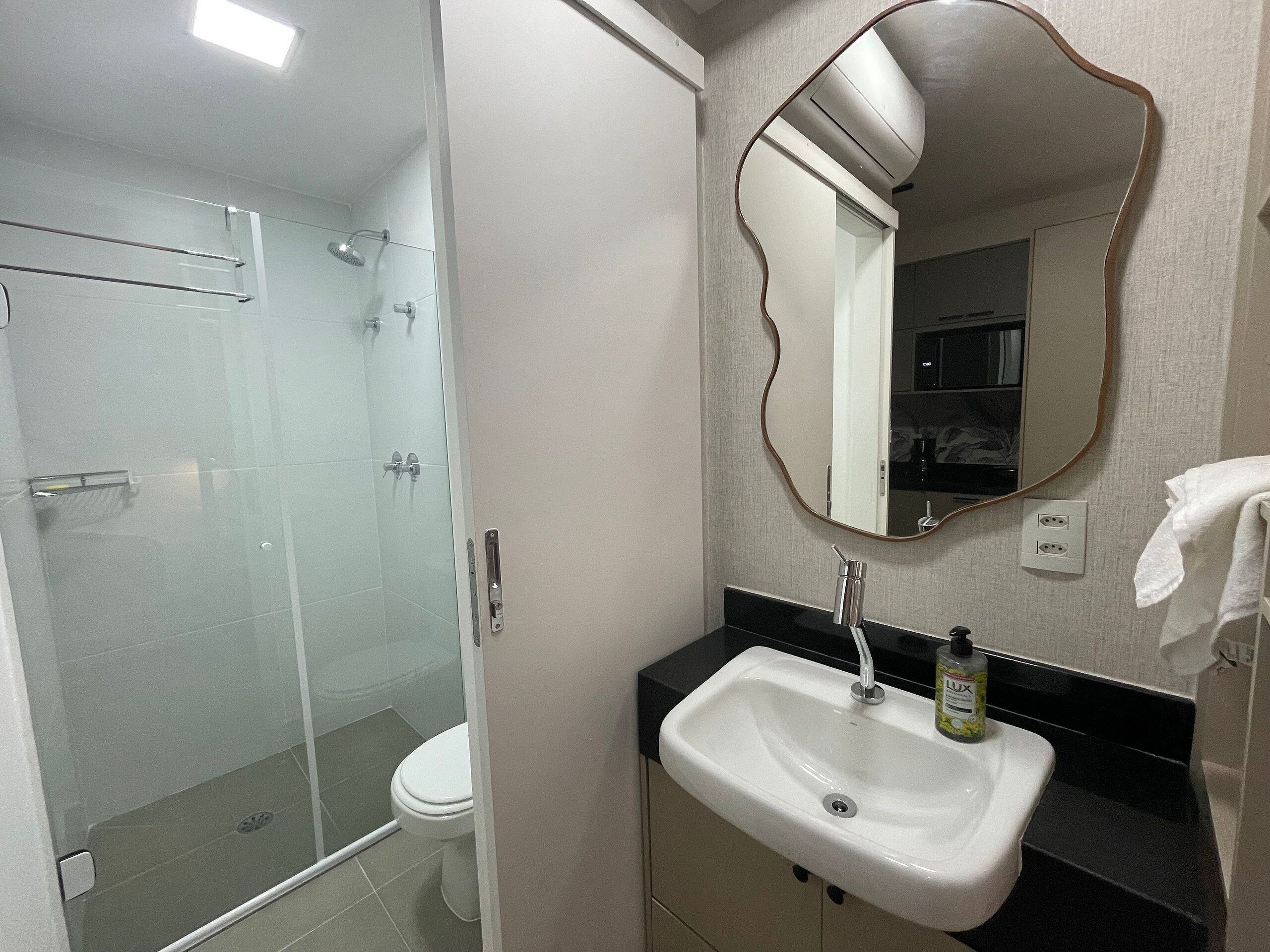 A bathroom with a glass-enclosed shower, a white toilet, a sink with a faucet, and a mirror with a wavy frame.
