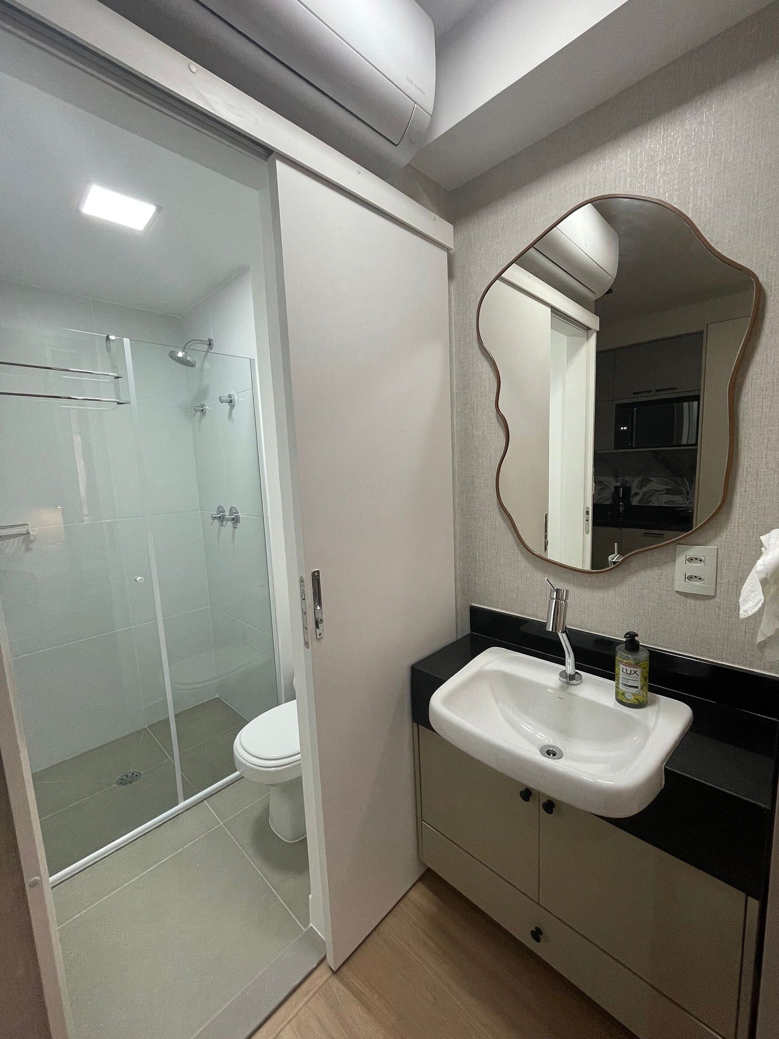 A bathroom with a glass shower enclosure, a white toilet, a sink with a black countertop, and a mirror with a wavy frame.