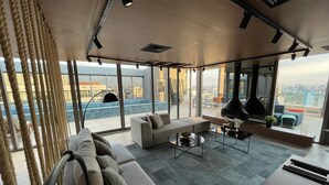 Una sala de estar moderna con un sofá, una mesa de centro y vistas de la ciudad a través de amplias ventanas.