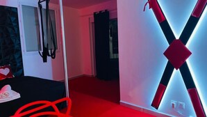 Une chambre d’hôtel avec une moquette rouge, un lit avec un oreiller blanc, une tête de lit noire et un luminaire fixé au mur.