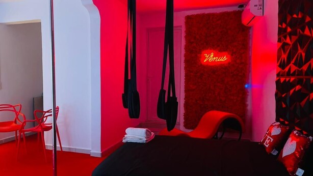 Une pièce avec un tapis rouge, un lit, une chaise et un panneau lumineux au néon sur le mur.