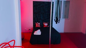 Une chambre avec un lit, deux oreillers ornés du mot « AMOUR », une serviette roulée et une fenêtre avec des stores.
