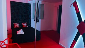 Une chambre d’hôtel avec un lit noir, des oreillers rouges, une chaise rouge et un motif géométrique sur le mur.