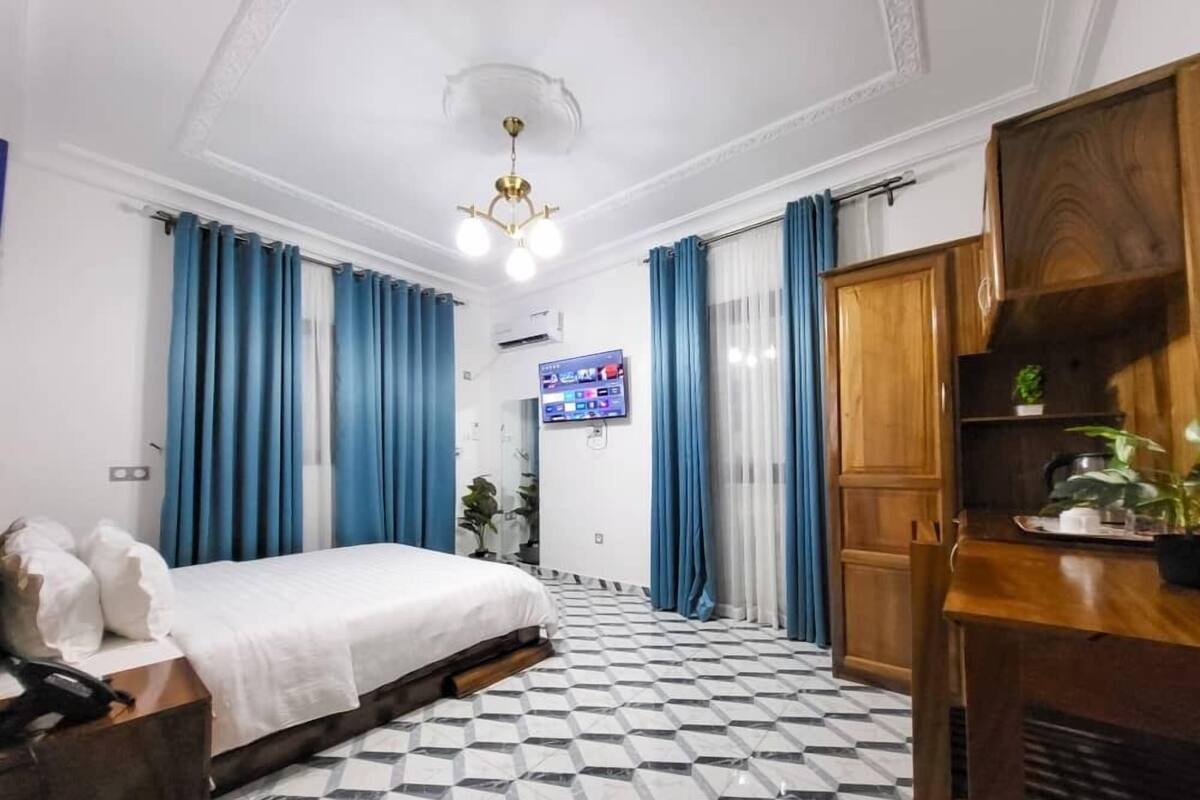 A hotel room with a bed, a TV, a wooden cabinet, and a check-in counter.