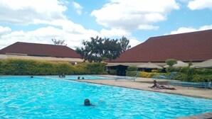 Une piscine où une personne nage, entourée d’un espace paysager avec des arbres et d’un bâtiment doté d’un toit rouge.