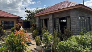 Une maison en pierre avec un toit rouge, entourée de différentes plantes en pot et d’un jardin.