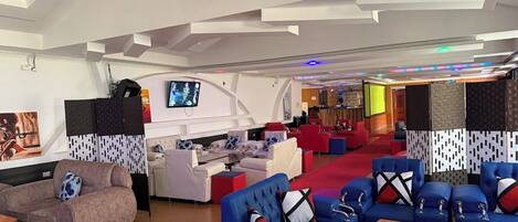 A modern lounge area with sofas and chairs, a television, and a bar area.