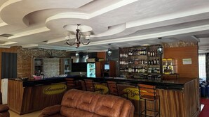 Un espace bar avec un comptoir, des tabourets et un canapé en cuir. On y trouve des étagères remplies de bouteilles et un réfrigérateur.