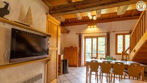 Una habitación acogedora con techo de madera, televisor, mesa de comedor con sillas y ventana con cortinas.