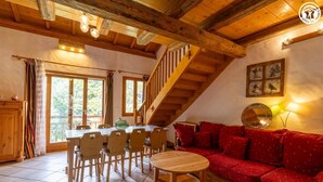 Una habitación acogedora con una escalera de madera, una mesa de comedor con sillas, un sofá rojo y un espejo grande.