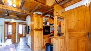 Cocina de madera con microondas, horno y armarios. Hay un bote de basura y una ventana con vistas al exterior.