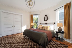 A bedroom with a large bed, two bedside lamps, a window with curtains, a wall-mounted ring light, and a checkered rug. - The Old Fashioned | Hot Tub, Fire Pit, Mini Golf Steps From Bardstown Rd (Louisville)