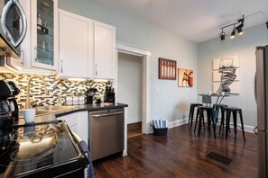 A modern kitchen with white cabinets, a black countertop, and a dishwasher. There is a dining area with a table and chairs.