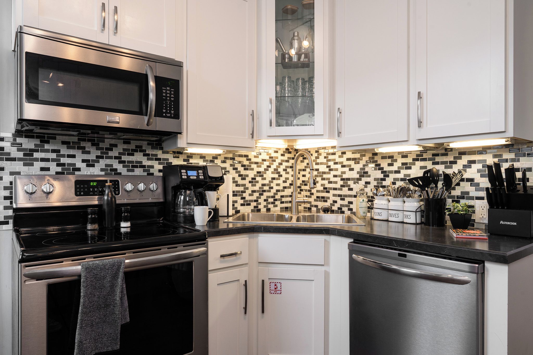 A modern kitchen with stainless steel appliances, white cabinets, and a black and white tiled backsplash.