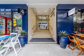 Entrada de hotel con refrigerador Coca-Cola, una escalera y un área de descanso con sillas y mesas de madera.