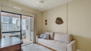 Una sala de estar moderna con un sofá, una mesa de centro de madera y vistas de la ciudad a través de grandes ventanales.