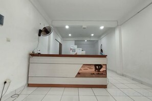 Zona de recepción de un hotel con mostrador, ventilador y piso de baldosas.