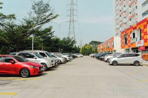 A parking lot with cars parked in rows, a building with a checkered facade, and power lines in the background. - Aurora Rooms at Apartment Mahakam (North Cikarang)