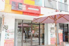Entrada de hotel con puerta de vidrio, un letrero que dice 'ROOM FOLD 99' y un balcón con barandilla.