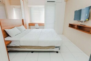 A bedroom with a bed, a TV mounted on the wall, and a window with blinds. - Aurora Rooms at Apartment Mahakam (North Cikarang)