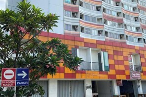 Un edificio de varios pisos con fachada a cuadros, un letrero que indica el camino a un parque y un escaparate visible con un cartel.
