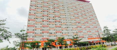 Ein mehrstöckiges Hotel mit einheitlicher Fassade, Balkonen und einer begrünten Anlage mit Bäumen und Sträuchern.