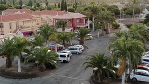 A residential area with parked cars, palm trees, and buildings with red and beige facades.