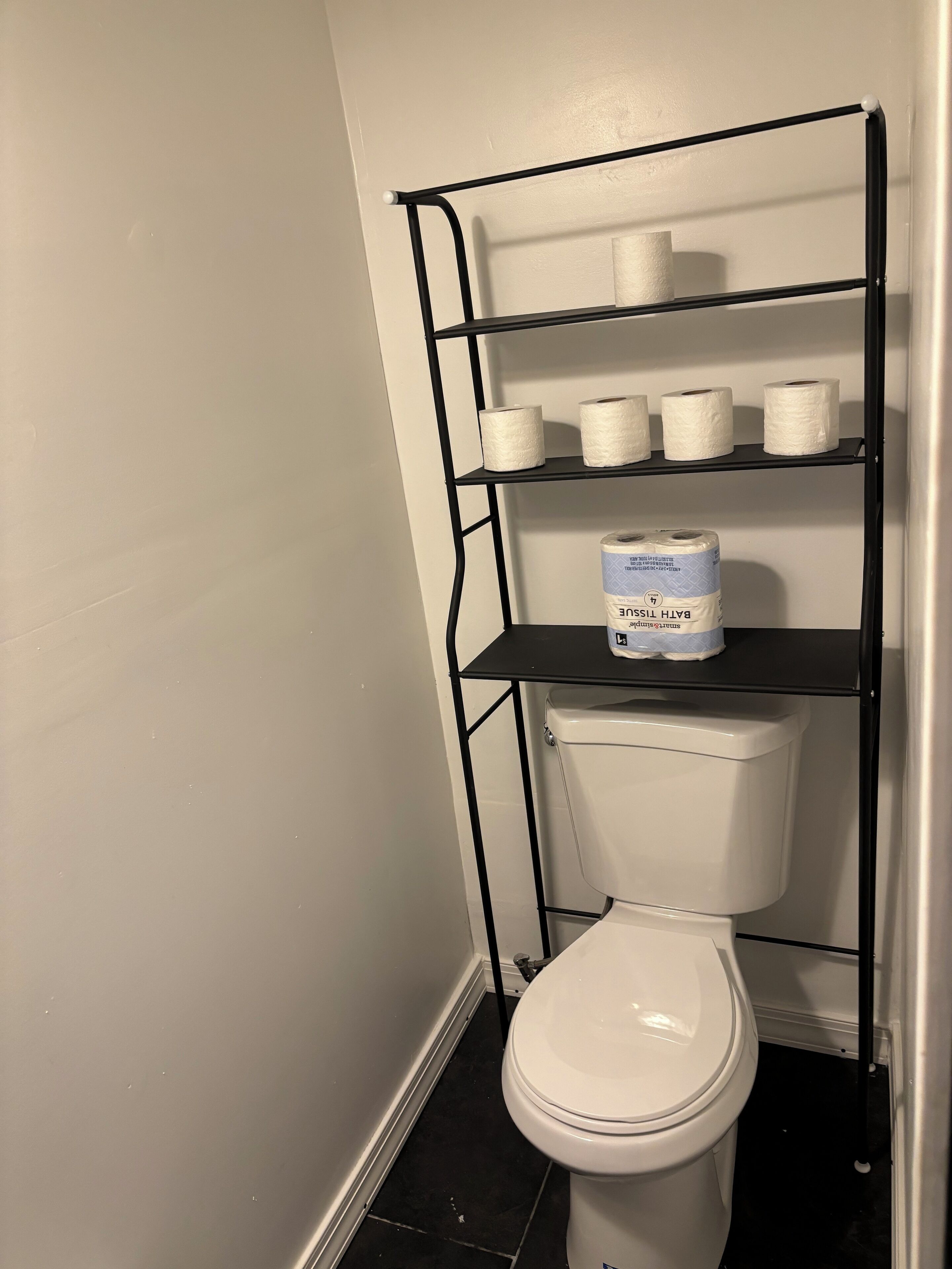 Toilet med en sort metalklappe over, hvor toiletpapirruller står.