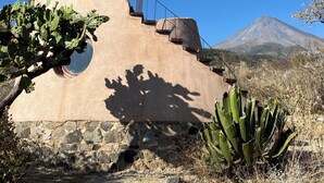 A building with a unique architectural design, featuring a circular window and a staircase leading to a flat roof. - Volcancito del Oeste (La Yerbabuena)