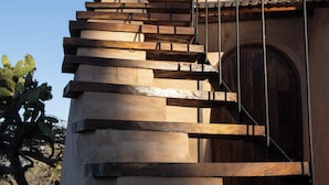 A spiral staircase leading to a wooden door, with a metal railing on the upper landing. - Volcancito del Oeste (La Yerbabuena)