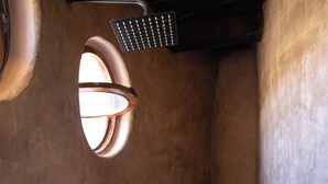 A rustic bathroom with a stone accent wall, a built-in shower, and a small shelf with toiletries. - Volcancito del Oeste (La Yerbabuena)