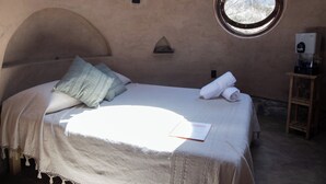 A bedroom with a bed, pillows, a towel, a small table with a water dispenser, and a window. - Volcancito del Oeste (La Yerbabuena)