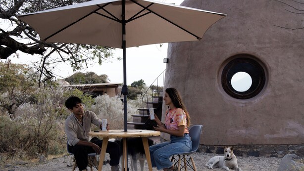 Two people sitting at a round table under an umbrella, with a dog lying nearby. - Volcancito del Oeste (La Yerbabuena)