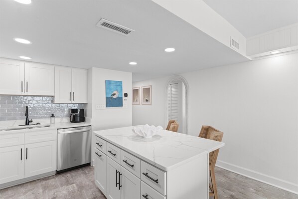 A modern kitchen with white cabinetry, a stainless dishwasher, and a marble island.