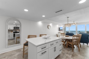Une cuisine moderne avec des meubles blancs, un îlot central et un coin repas comprenant des chaises en bois et un canapé bleu.