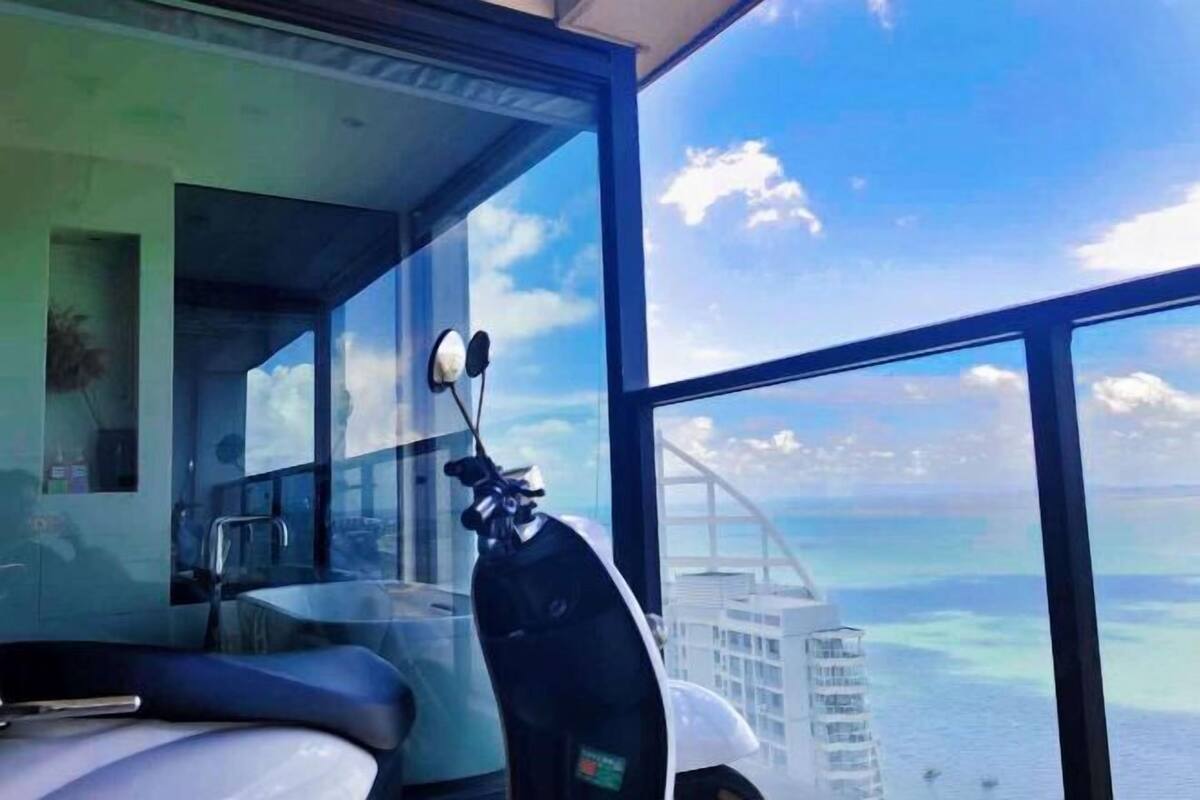 Une chambre moderne avec une grande fenêtre, un scooter et une vue sur un pont et sur l’eau.