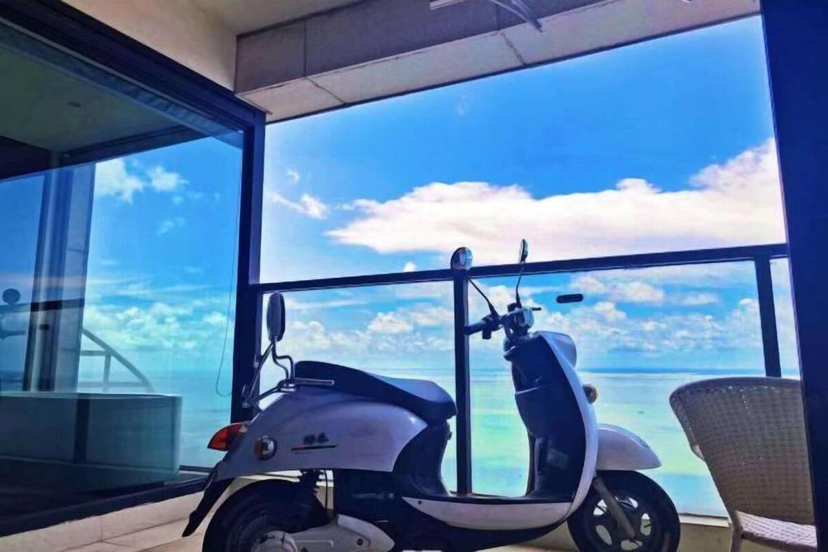 Un scooter est garé près d’une grande fenêtre donnant sur une plage.