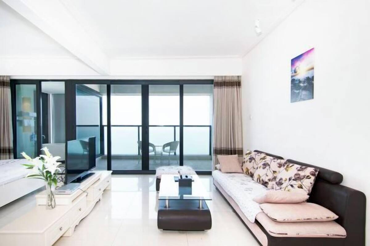 Un salon moderne avec un canapé, une table basse et un téléviseur. Il y a un balcon avec vue.