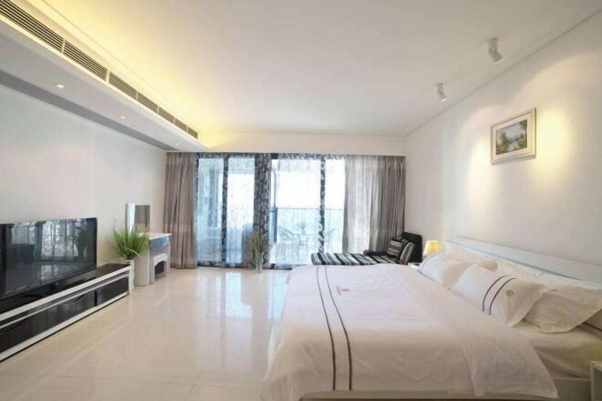 Une chambre d’hôtel moderne dotée d’un grand lit, d’une télévision à écran plat, d’un petit coin salon et d’un balcon avec des rideaux.