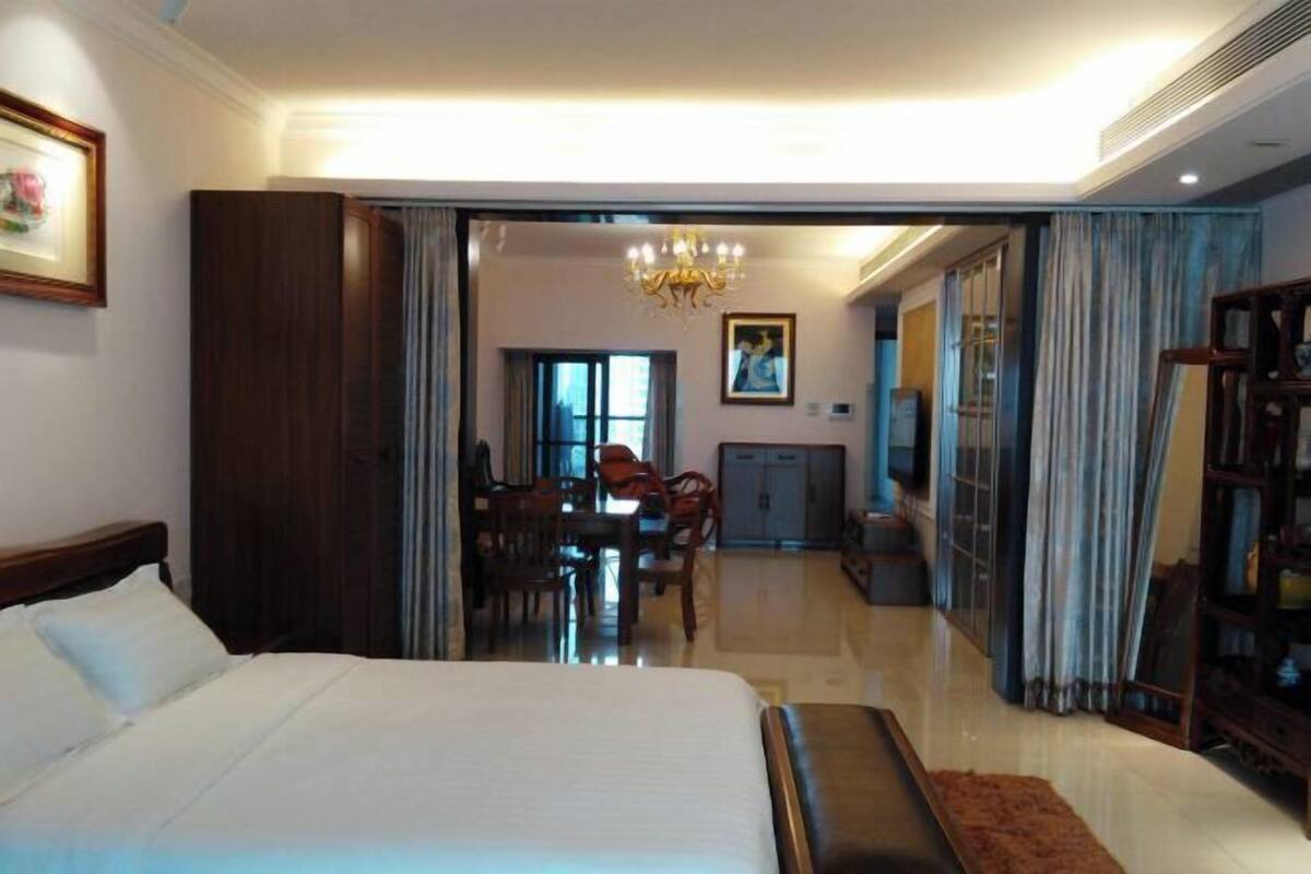 Une chambre d’hôtel avec un lit, un bureau et un coin repas, visibles à travers une porte ouverte.