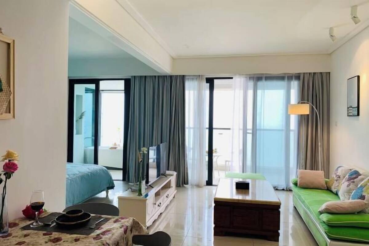 Une chambre d’hôtel moderne avec un lit, un canapé vert, une petite table et un téléviseur.