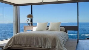 A bed with a view of the sea, a nightstand with a decorative item, and a large window. - One Room One Car Seaview Holiday Apartment (Beihai)