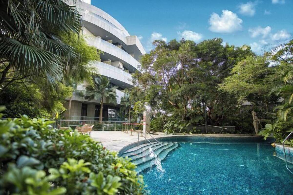 Un bâtiment moderne doté d’une piscine, le tout entouré d’une végétation luxuriante.