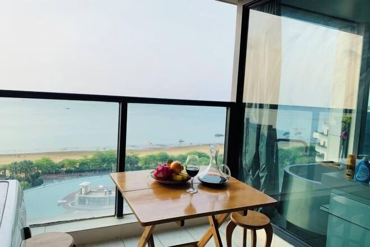 Un balcon avec une table, une chaise et une vue sur une étendue d’eau et la verdure.