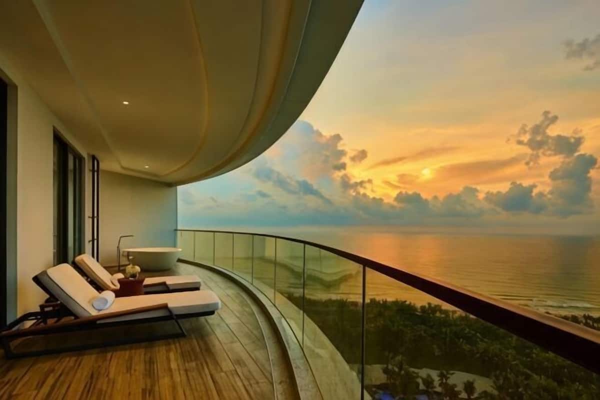 A balcony with a curved railing overlooking a body of water during sunset.