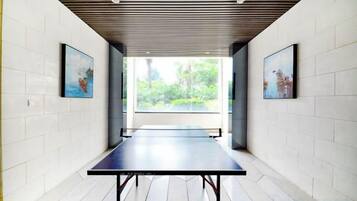 Un pasillo con mesa de ping pong, paredes de azulejos blancos y cuadros enmarcados.