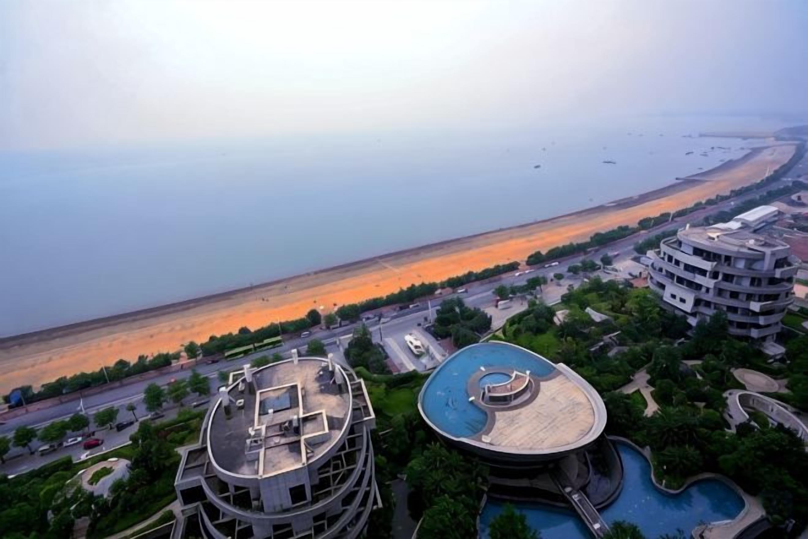 A coastal hotel with a pool, a view of the beach, and a parking area.