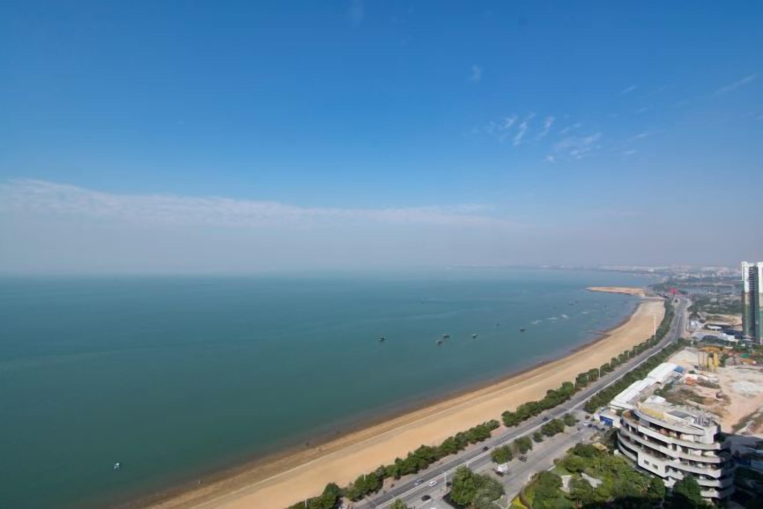 A coastal view with a beach, a road, and buildings.